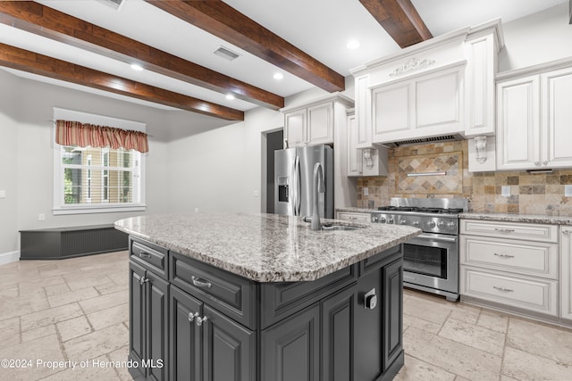 kitchen featuring light stone counters, a kitchen island with sink, beamed ceiling, white cabinetry, and appliances with stainless steel finishes