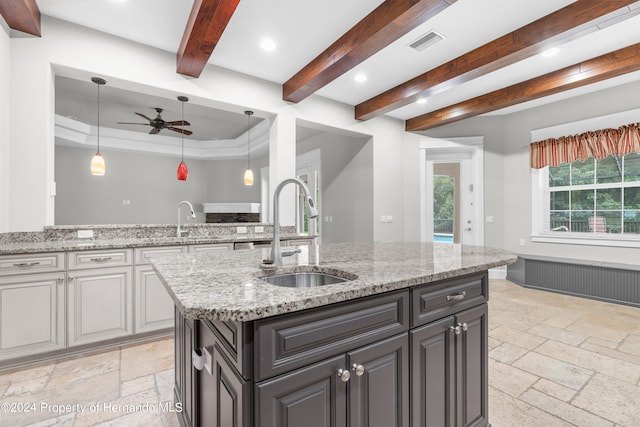 kitchen featuring sink, light stone countertops, beam ceiling, a kitchen island with sink, and pendant lighting