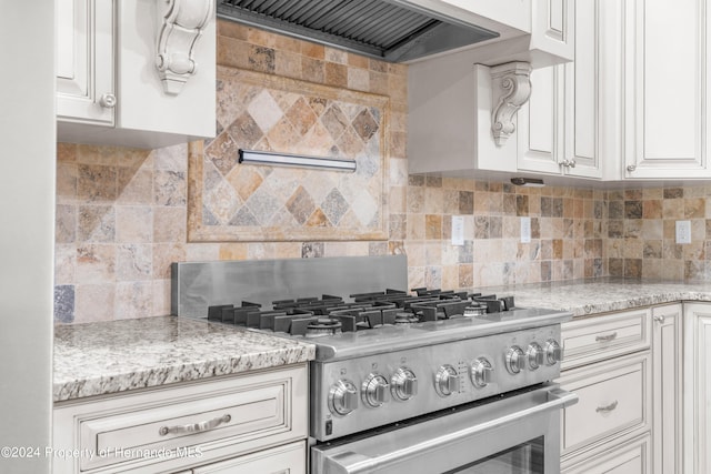 kitchen with light stone counters, white cabinets, decorative backsplash, ventilation hood, and high end stainless steel range