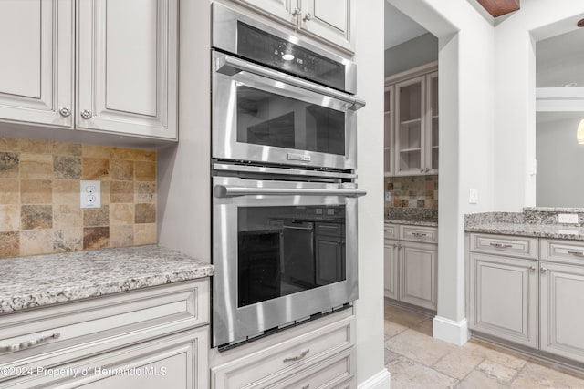 kitchen featuring stainless steel double oven, light stone counters, and backsplash