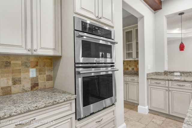 kitchen with decorative light fixtures, backsplash, stainless steel double oven, and light stone countertops