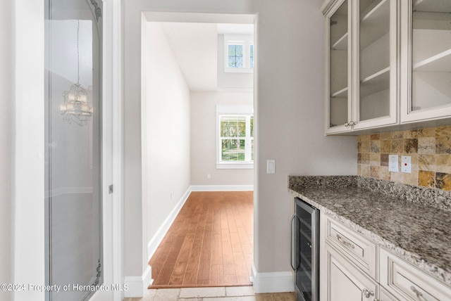 bar with light wood-type flooring, light stone counters, backsplash, and wine cooler