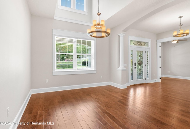 spare room featuring wood-type flooring, ornate columns, and ceiling fan with notable chandelier