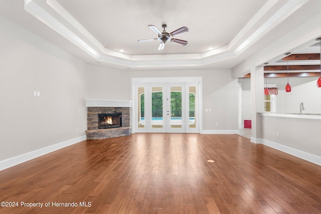 unfurnished living room featuring ceiling fan, a fireplace, wood-type flooring, a raised ceiling, and french doors