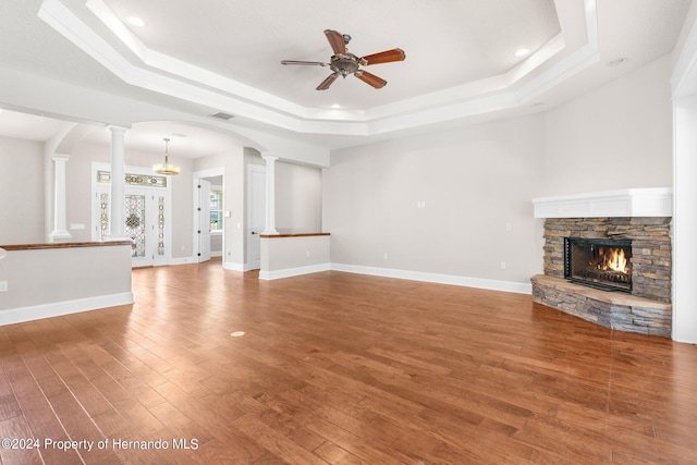 unfurnished living room featuring a fireplace, hardwood / wood-style flooring, ornate columns, and a raised ceiling