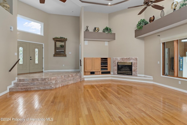 unfurnished living room featuring a towering ceiling, light wood-type flooring, ceiling fan, and a premium fireplace