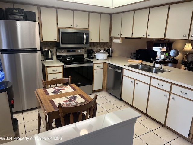 kitchen featuring white cabinets, sink, light tile patterned floors, backsplash, and appliances with stainless steel finishes