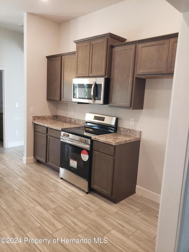 kitchen featuring light stone counters, dark brown cabinets, and stainless steel appliances