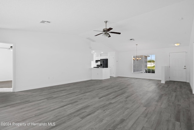 unfurnished living room with ceiling fan with notable chandelier, dark wood-type flooring, and vaulted ceiling