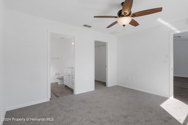 unfurnished bedroom with a closet, a walk in closet, light colored carpet, ceiling fan, and ensuite bathroom