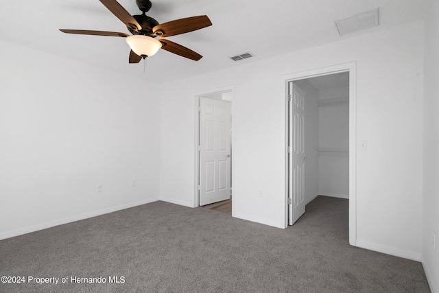 unfurnished bedroom featuring dark colored carpet, ceiling fan, a walk in closet, and a closet