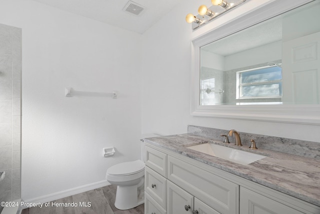 bathroom with tiled shower, vanity, hardwood / wood-style flooring, and toilet