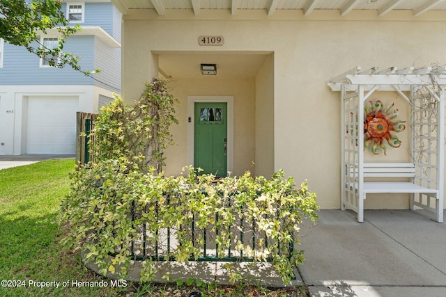 view of exterior entry featuring a garage and a pergola