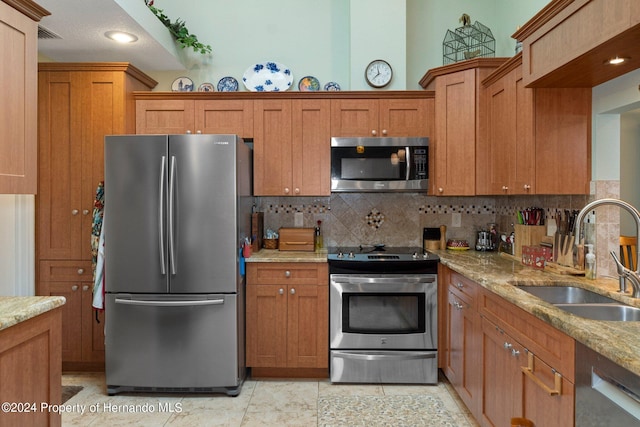 kitchen with decorative backsplash, light tile patterned floors, sink, light stone countertops, and appliances with stainless steel finishes