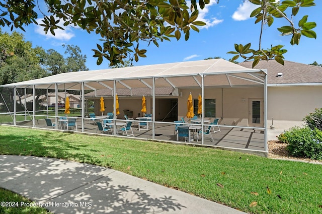 rear view of house with a lawn, glass enclosure, and a patio area