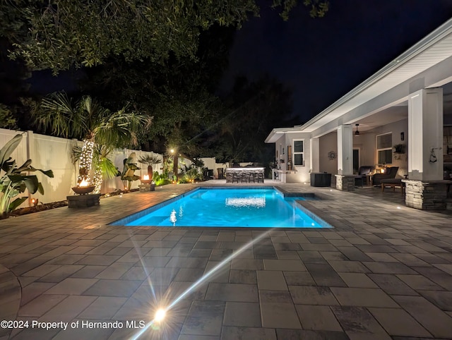 pool at night featuring a patio area