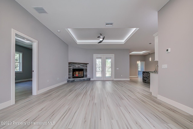 unfurnished living room with a stone fireplace, light wood-type flooring, and french doors