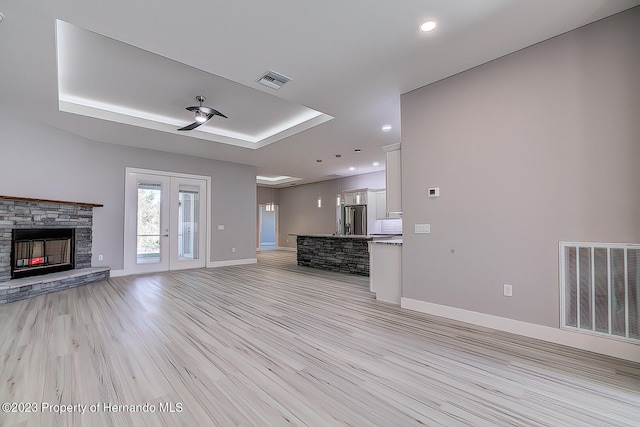 unfurnished living room featuring a fireplace, light wood-type flooring, french doors, and a tray ceiling