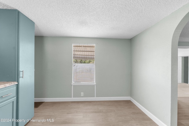 spare room featuring light wood-type flooring and a textured ceiling