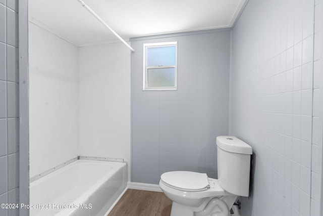 bathroom with tile walls, wood-type flooring, a bathing tub, and toilet