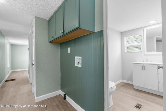 washroom featuring a textured ceiling, light wood-type flooring, hookup for a washing machine, and sink