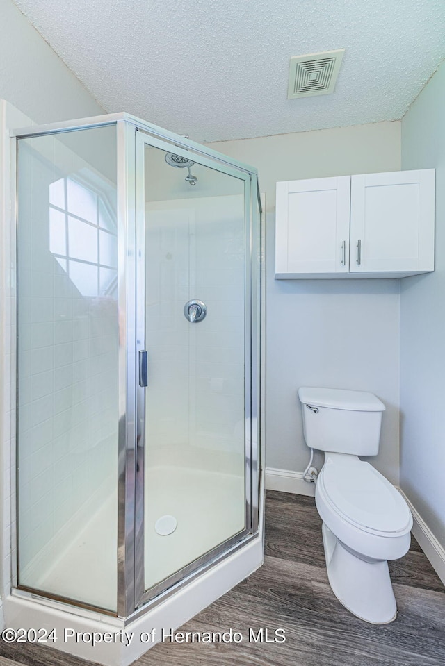 bathroom with hardwood / wood-style floors, a textured ceiling, toilet, and a shower with door