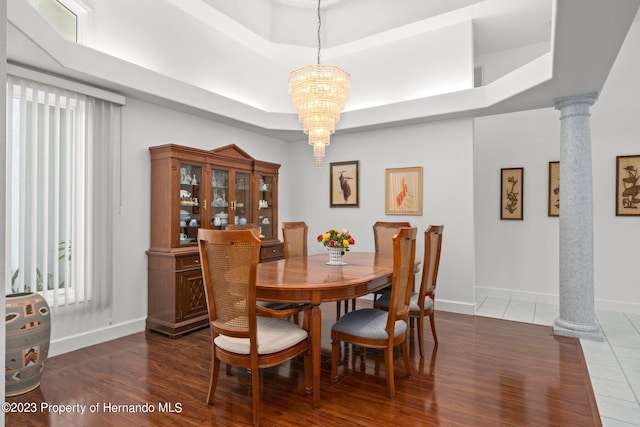 dining room with a tray ceiling, dark wood-type flooring, a chandelier, and decorative columns