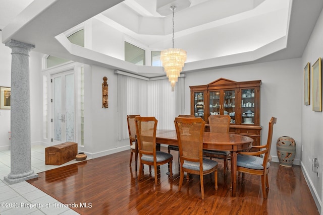 dining room with a tray ceiling, hardwood / wood-style flooring, ornate columns, and a notable chandelier