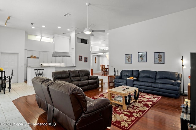 living room with a towering ceiling, ceiling fan, and light wood-type flooring