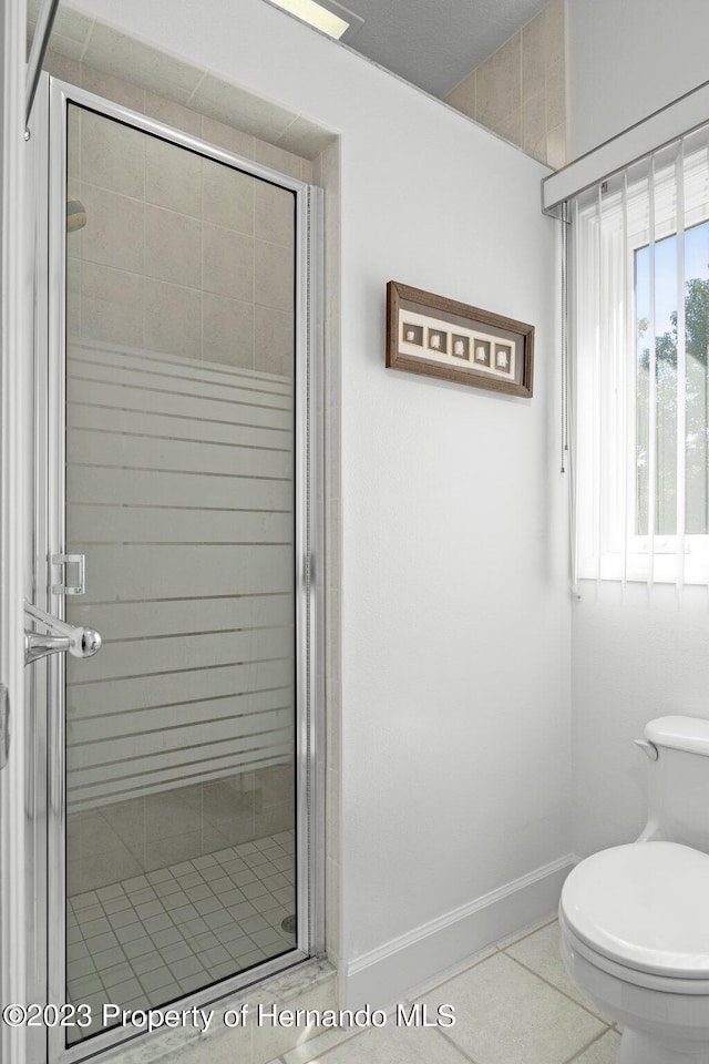 bathroom featuring tile patterned flooring, toilet, and a shower with door