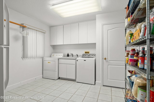 clothes washing area with cabinets, light tile patterned floors, washing machine and clothes dryer, and sink