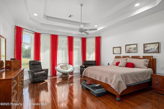 bedroom with dark hardwood / wood-style floors, ceiling fan, and a tray ceiling