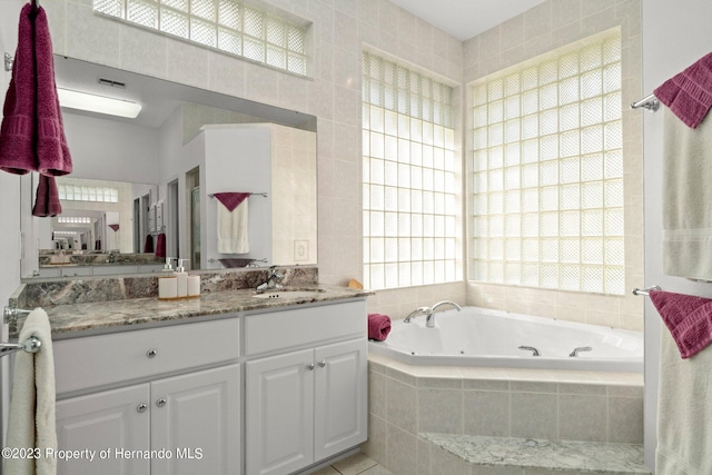 bathroom featuring tiled bath, a wealth of natural light, vanity, and tile walls