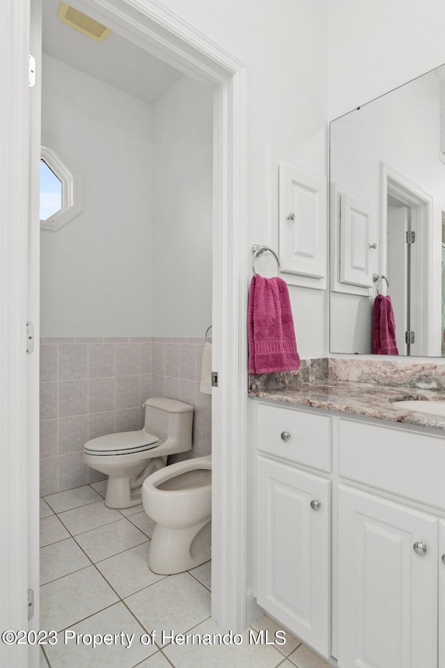 bathroom with a bidet, toilet, tile walls, tile patterned flooring, and vanity