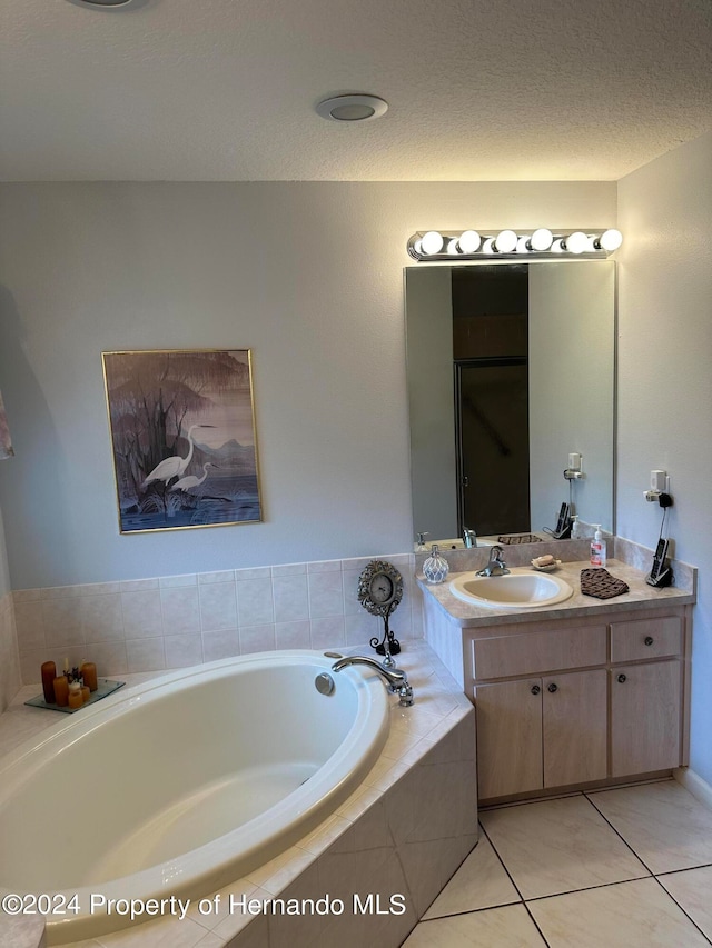 bathroom featuring tiled bath, tile patterned flooring, vanity, and a textured ceiling