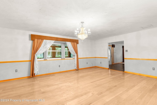 empty room with baseboards, wood finished floors, and a notable chandelier