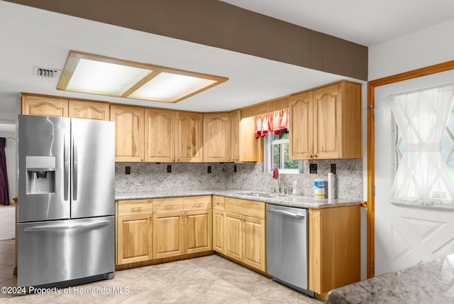 kitchen with stainless steel appliances, a sink, visible vents, light stone countertops, and tasteful backsplash