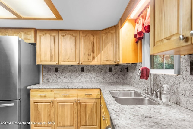 kitchen with light stone counters, backsplash, a sink, and freestanding refrigerator