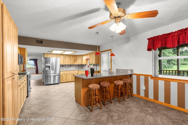 kitchen featuring stainless steel appliances, kitchen peninsula, dark stone counters, ceiling fan, and a breakfast bar area