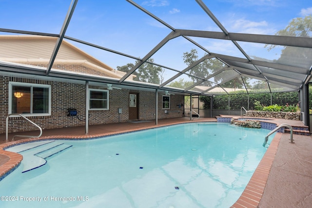 view of pool featuring glass enclosure, a pool with connected hot tub, and a patio area