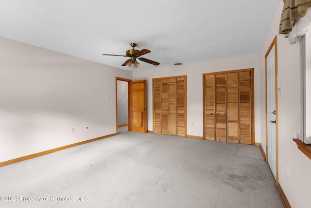 unfurnished bedroom with ceiling fan, two closets, and carpet