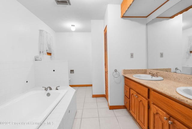 bathroom with vanity, tile patterned flooring, toilet, and a relaxing tiled tub