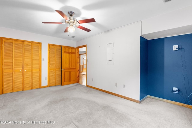 unfurnished bedroom with ceiling fan, multiple closets, and light colored carpet