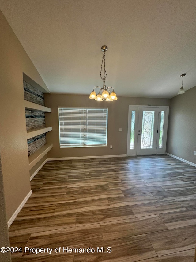 unfurnished dining area featuring a chandelier, hardwood / wood-style floors, a textured ceiling, and vaulted ceiling