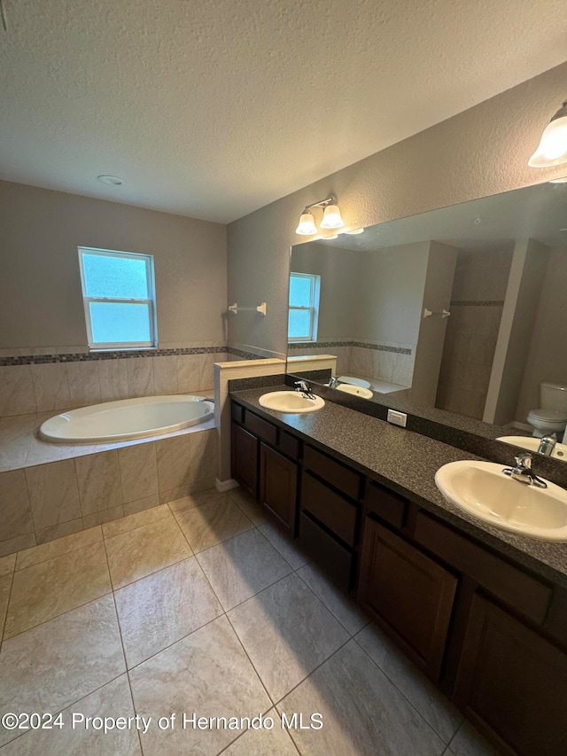 bathroom featuring tile patterned floors, tiled bath, a textured ceiling, toilet, and vanity