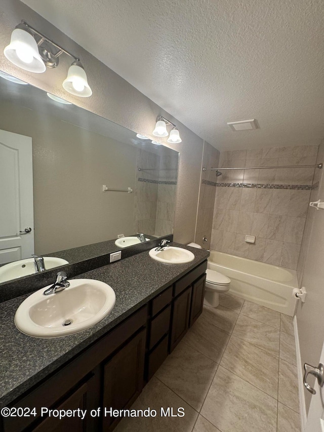 full bathroom featuring vanity, a textured ceiling, tiled shower / bath combo, tile patterned flooring, and toilet