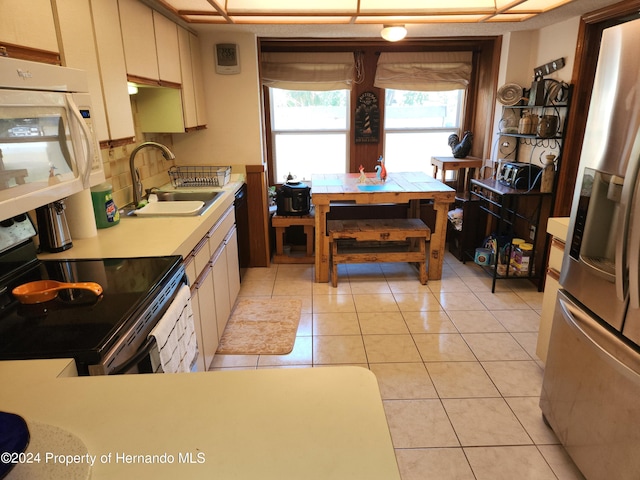 kitchen with stainless steel refrigerator with ice dispenser, sink, light tile patterned flooring, and electric range