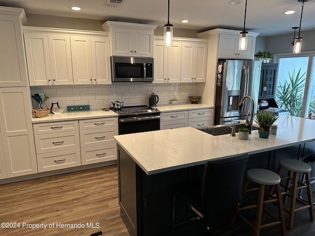 kitchen with white cabinetry, decorative light fixtures, a center island with sink, and stainless steel appliances