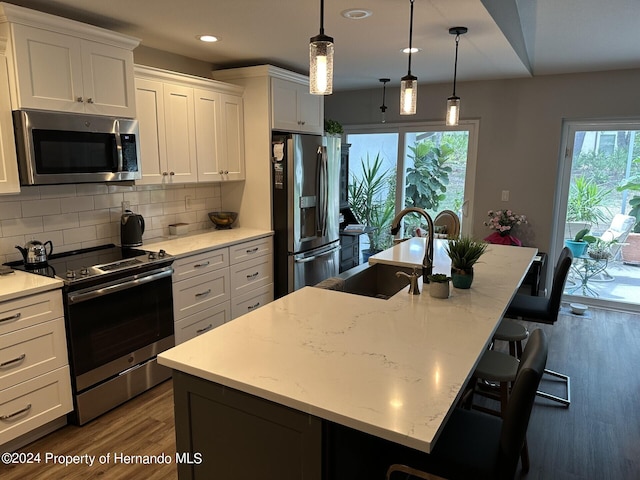 kitchen with stainless steel appliances, a center island with sink, white cabinetry, a breakfast bar, and pendant lighting