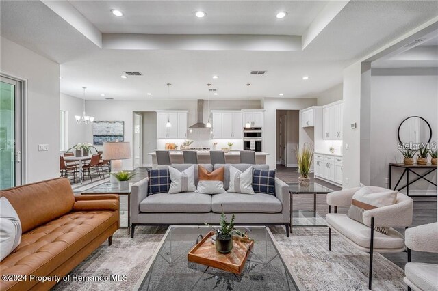 living room featuring a tray ceiling, an inviting chandelier, and wood-type flooring